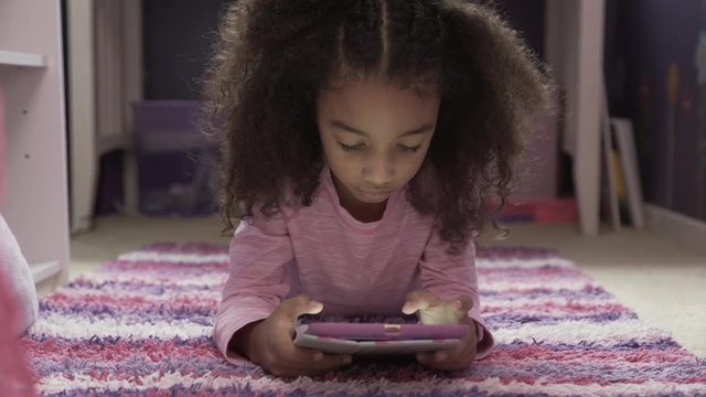 Dolly shot of girl using tablet computer while lying on rug at home