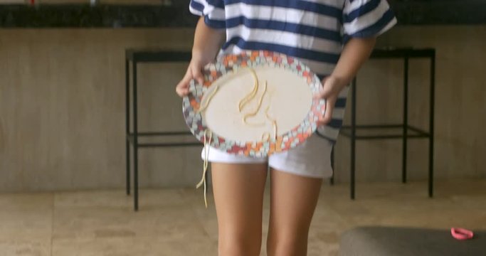 A young girl carrying a plate of spaghetti accidentally spills it on the floor