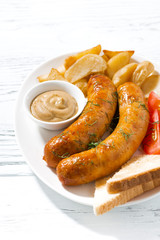 fried pork sausages with potatoes and mustard on white background, vertical closeup