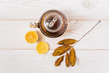 glass teapot with tea,lemon and leaves.white wooden background.top view