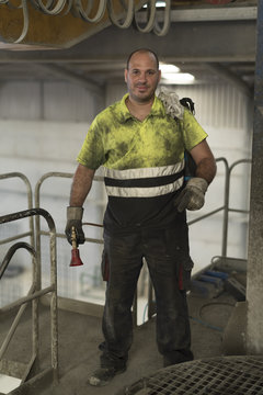 Construction worker man with non-stick liquid tank for industrial concrete mixers poses looking at camera. Real people in their work environment.