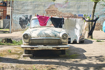 Old vintage car for parts in a Soviet style backyard where laundry is dried on a rope casting...