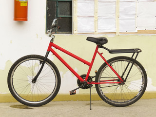 Fototapeta na wymiar Old and worn red bike, abandoned leaning against the wall too worn