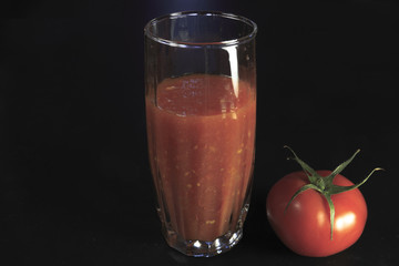 Fresh tomatoes and glass of tomato juice isolated on dark background. Vegan food.