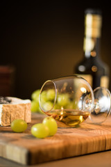 Still life of grapes, Cognac and french cheese on a wooden board
