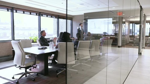 Dolly shot of business people discussing in board room seen through glass
