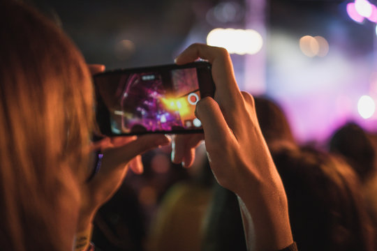 woman using mobile phone taking photo of live show concert with blurry stage as background. have a copy space for text.