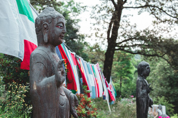 two statues of buddha in a garden connected by different national flags