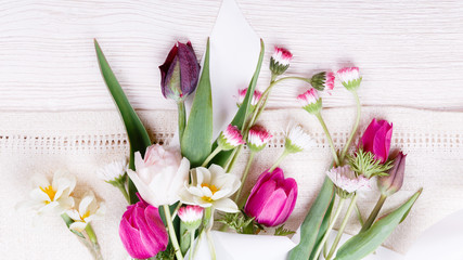 Fototapeta premium Bouquet first spring flowers, pink, purple tulips, daffodils and daisies on white wooden background.