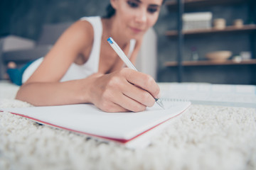 Close up portrait of woman hand with pencil writing in copybook, blurred background of girl laying on stomach on carpet