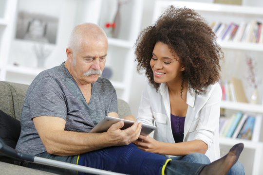 carer and senior man with tablet sitting on the sofa