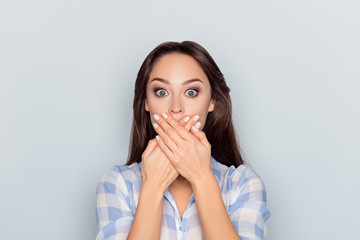 Close up portrait of attractive, pretty, cute, charming, woman closed her mouth with crossed hands and wide opened eyes, looking at camera, she can't believe her eyes, standing over grey background