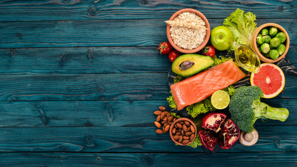 Obraz na płótnie Canvas Healthy food. Fish salmon, avocado, broccoli, fresh vegetables, nuts and fruits. On a wooden background. Top view. Copy space.