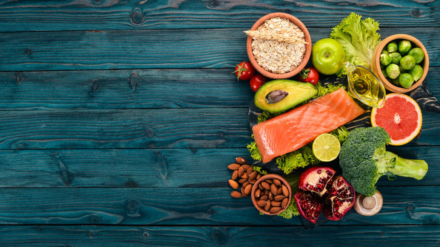 Healthy Food. Fish Salmon, Avocado, Broccoli, Fresh Vegetables, Nuts And Fruits. On A Wooden Background. Top View. Copy Space.