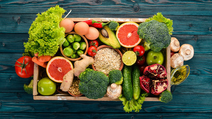 The concept of healthy food. Fresh vegetables, nuts and fruits in a wooden box. On a wooden background. Top view. Copy space.
