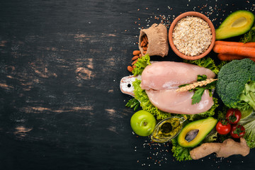 Healthy food. Chicken fillet, avocado, broccoli, fresh vegetables, nuts and fruits. On a wooden background. Top view. Copy space.