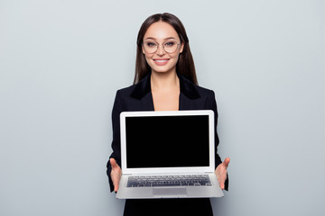 Portrait with copy space of pretty, cheerful, confident, professional, elegant, brunette in jacket demonstrating black screen and keypad of open laptop, standing over grey background