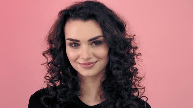 Beautiful fashionable girl with long curly hair in a black T-shirt. Girl in the studio on a pink background.Advertising, hair products, beauty salon, cosmetics, clothing. Fashion, boutique. Pink.