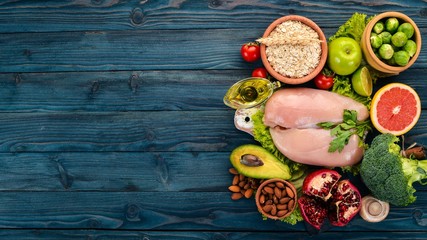 Healthy food. Chicken fillet, avocado, broccoli, fresh vegetables, nuts and fruits. On a wooden background. Top view. Copy space.