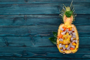 Exotic fruit salad served in half a pineapple. Papaya, Dragon Fruit, tamarind, cactus fruit, mango, mangosteen On a wooden background. Top view.