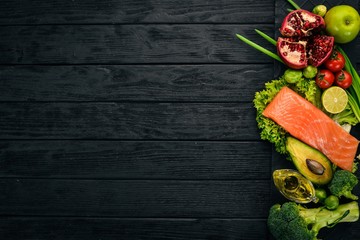 Healthy food. Fish salmon, avocado, broccoli, fresh vegetables, nuts and fruits. On a black background. Top view. Copy space.
