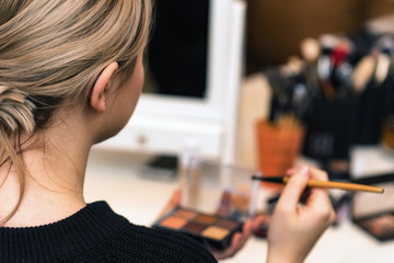 Back view teenage girl applies makeup with brush