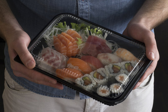 Manos sujetando contenedor de sushi delivery,comida japonesa.