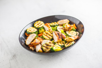 Grilled chicken breast zucchini broccoli and carrot in black plate. Greek or mediterranean food