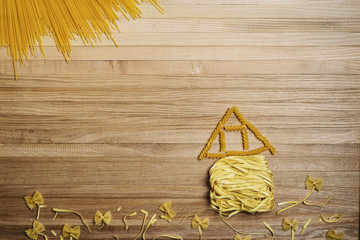Landscape with house, flowers and sun from spaghetti and pasta on a wooden background