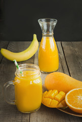 Mango and orange juice in mason jar and slice of tropical fruits on wooden table. Fresh healthy tropical drink.