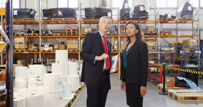 4K Business man & woman discussing inventory in large storage warehouse. Slow motion.