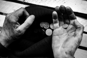 The beggar considers coins. A beggar on the street is holding dirty hands with money