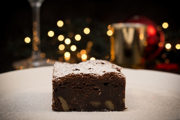 CHRISTMAS BROWNIE DESSERT SERVED IN A WHITE PLATE AND CHRISTMAS LIGHTS BACKGROUND
