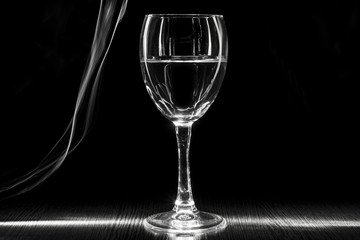 A transparent glass of wine with a liquid. White blurred stripes on a black background.