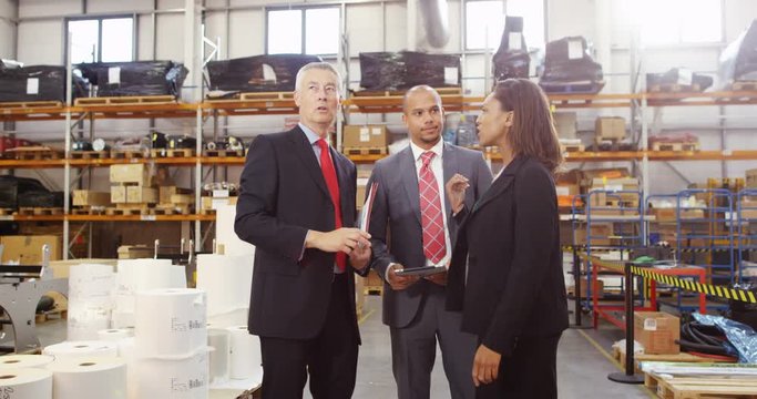 4K Business group in factory warehouse looking at computer tablet & discussing inventory. Slow motion.