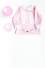 Cute pink baby clothes for girl. Shirt, toy, bottle on white background top view copy space