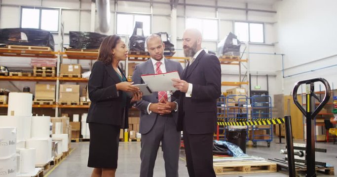 4K Businesswoman negotiating a deal with investors in factory warehouse, looking at computer tablet & discussing inventory. Slow motion.
