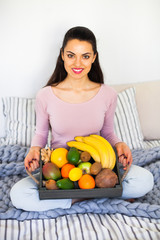 Young girl wearing pastel colored home clothes with tray full of fresh fruit. Summer healthy raw vegan clean eating breakfast in bed concept. Top view, copy space