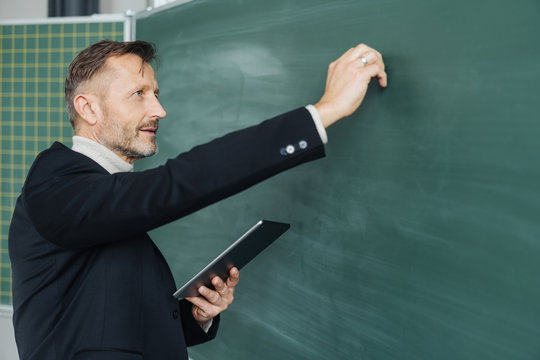 Middle-aged male teacher writing on a chalkboard