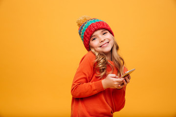 Smiling Young girl in sweater and hat holding smartphone