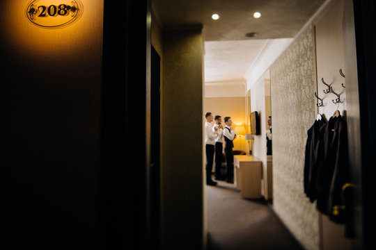 stylish groomsmen helping happy groom getting ready in the morning for wedding ceremony. luxury man in suit in room.
