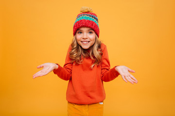 Smiling Young girl in sweater and hat shrugs her shoulders