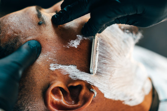 Close up of barber shaving beard of customer