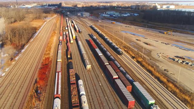Looking down on industrial railroad train yard, many trains, tracks. Dynamic aerial view.
