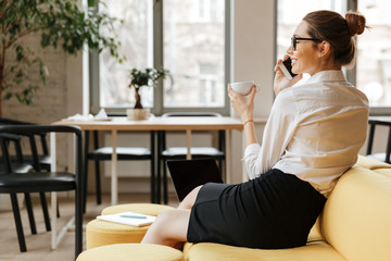 Cheerful business woman talking by phone drinking coffee