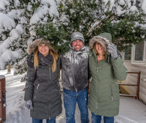 Three Young Adults Play In The Snow Behind A House As They Cover One Another And Cause Mischief With The Snow