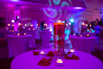 Glass vase with red roses water and light candles
