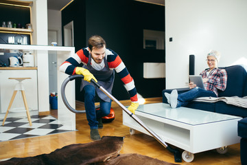 Handsome husband cleaning house while his pregnant wife relaxing on sofa.