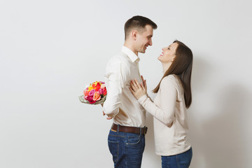 Couple in love. Woman looking behind man who hiding behind him bouquet of beautiful roses flowers isolated on white background. St. Valentine's Day, International Women's Day birthday holiday concept