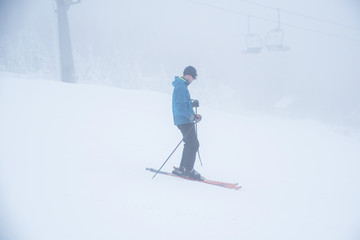 Naklejka na ściany i meble Skier silhouette in white ski resort. Fog in background
